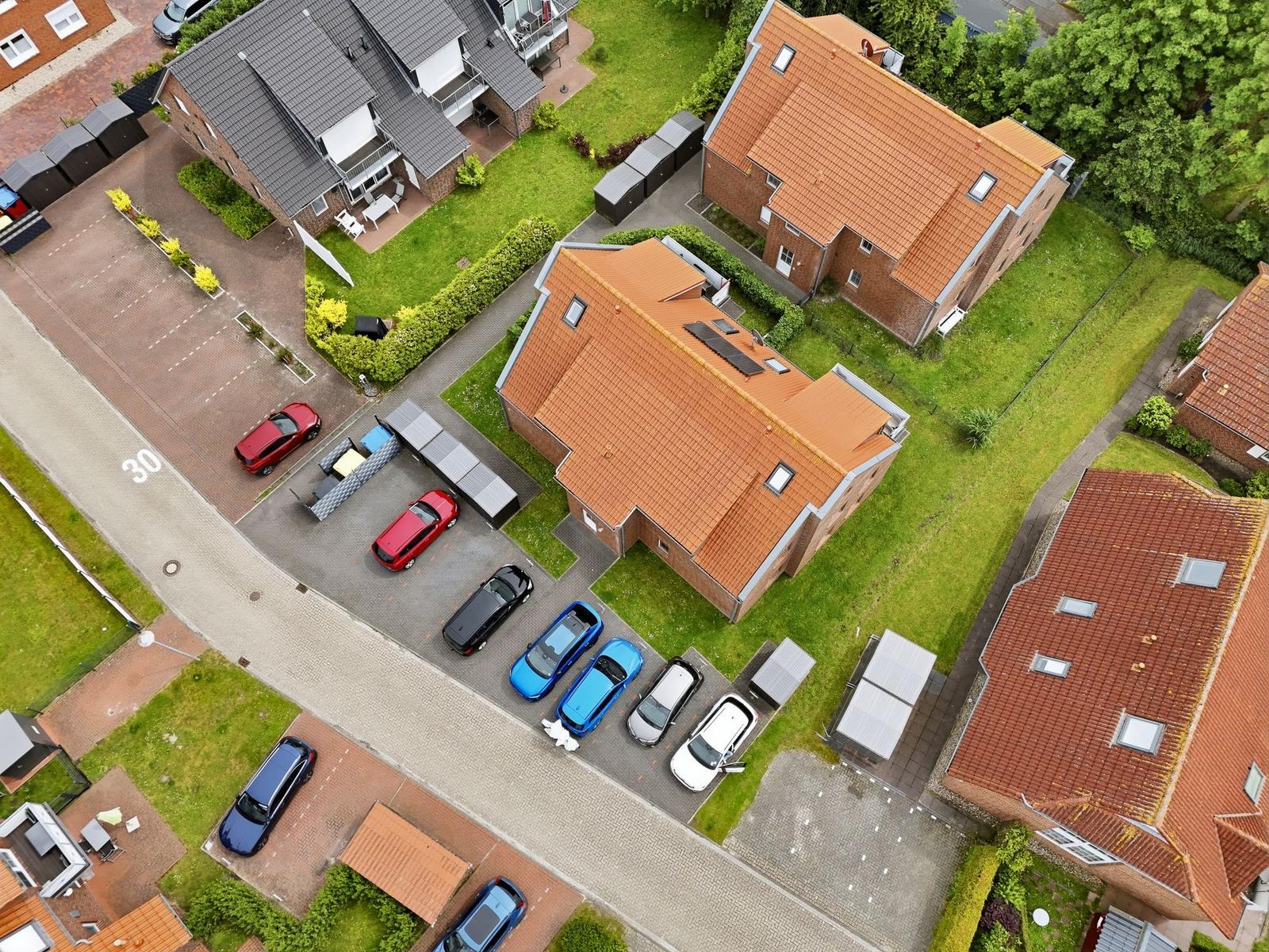 Aerial view of several houses with red roofs and parked cars on the property.