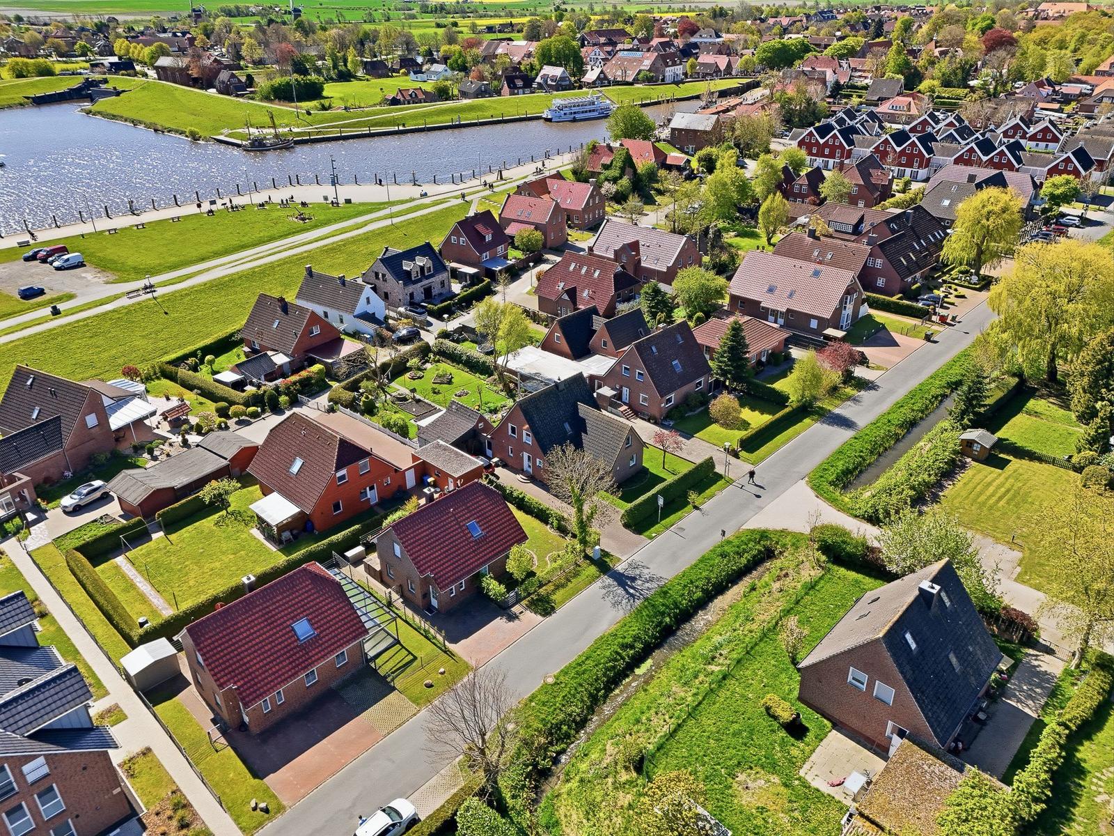 Aerial view of a village with houses, green areas, and a river.