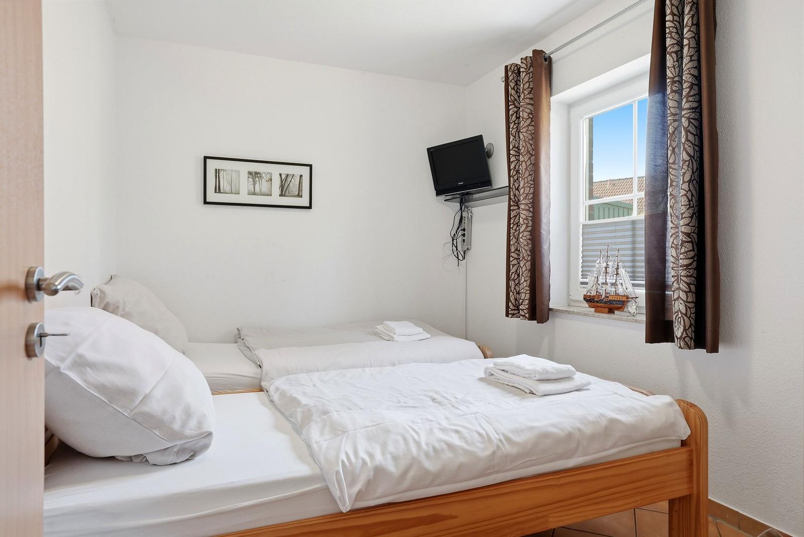 Zwei Betten mit weißen Bettwäsche, Wand-TV und Fenster mit Segelschiffmodell.