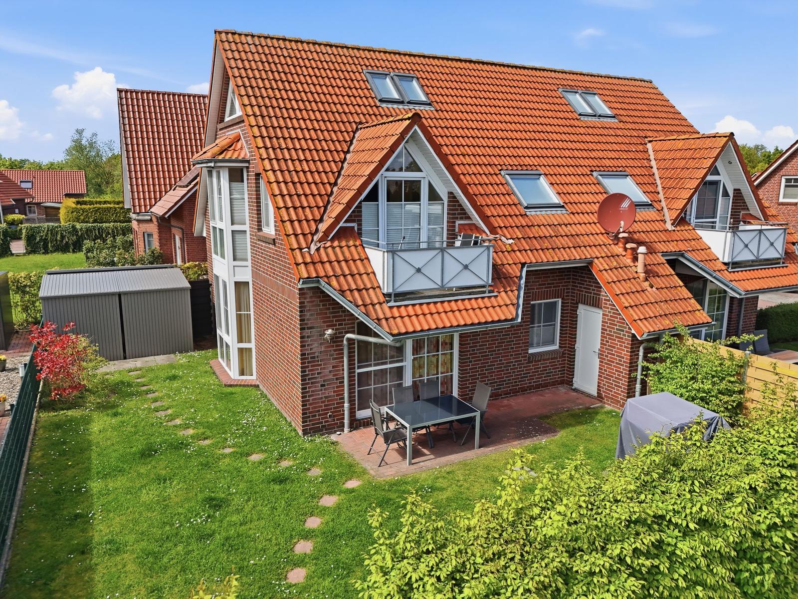 Ein zweistöckiges Haus mit rotem Dach und Balkon. Garten mit Tisch und Stühlen.