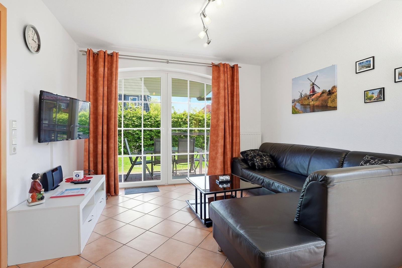 Wohnzimmer mit Sofa, Fernseher und Terrasse mit Gartenblick.