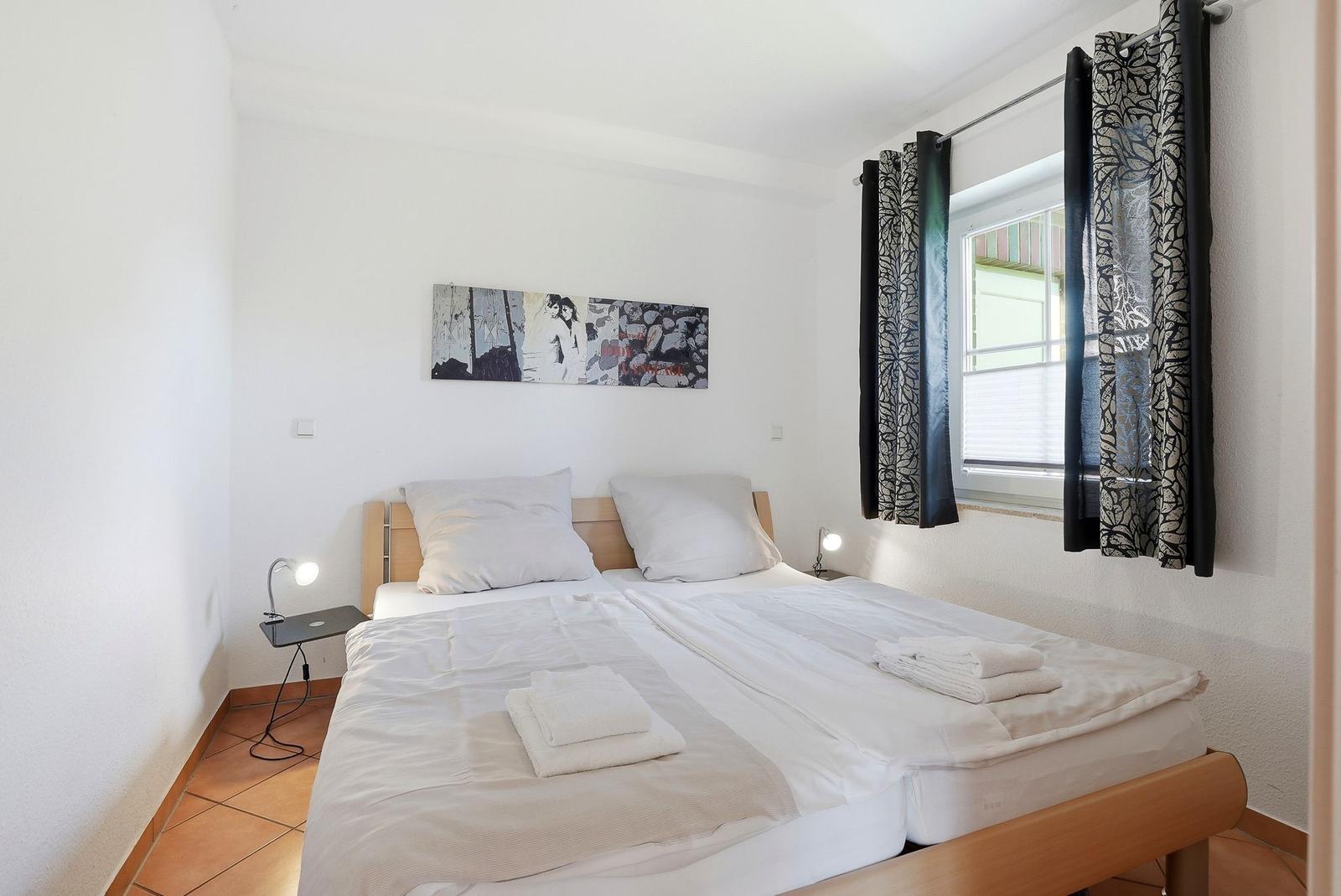 Schlafzimmer mit Doppelbett, Fenster und Wandbild.