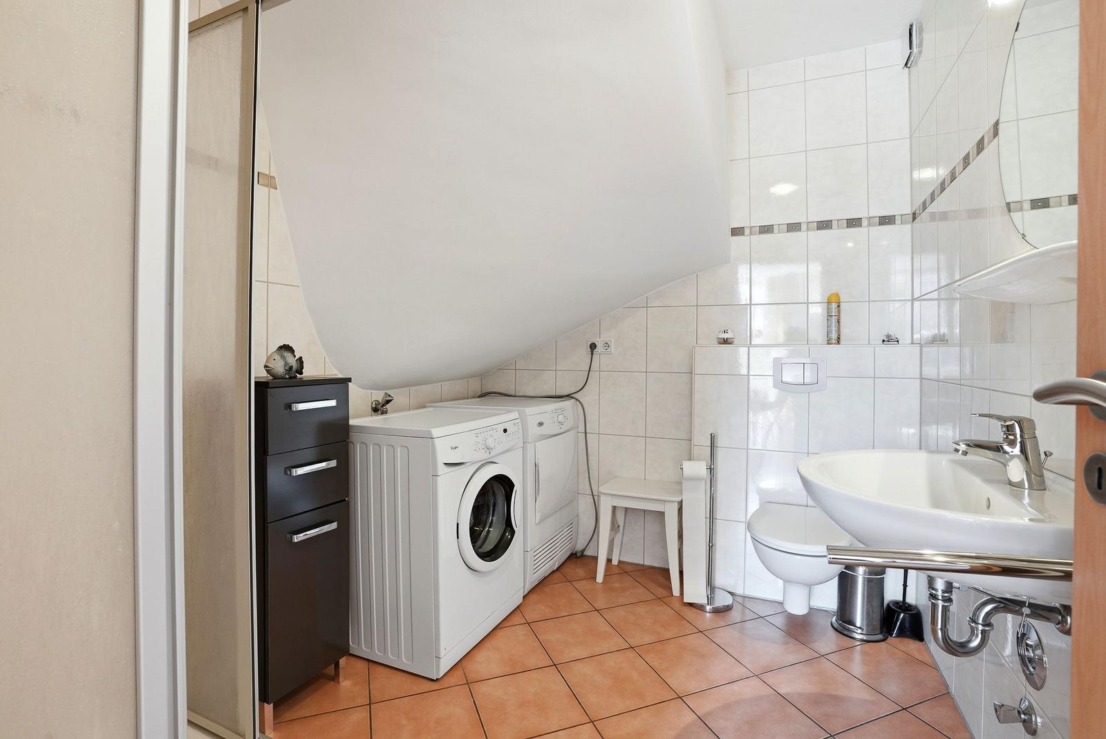 Badezimmer mit Waschmaschine, Toilette und Waschbecken.