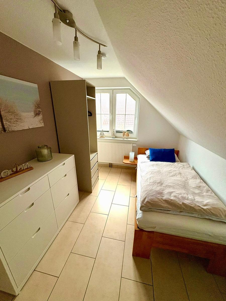 Schlafzimmer mit Dachschräge, Bett, Schrank und Fenster.