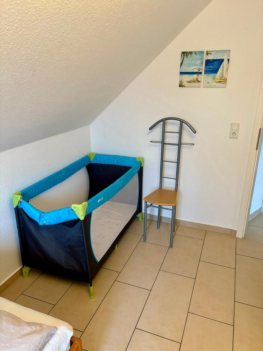 Kinderbett und Kleiderständer in einem Zimmer mit schräger Decke und Bodenfliesen.