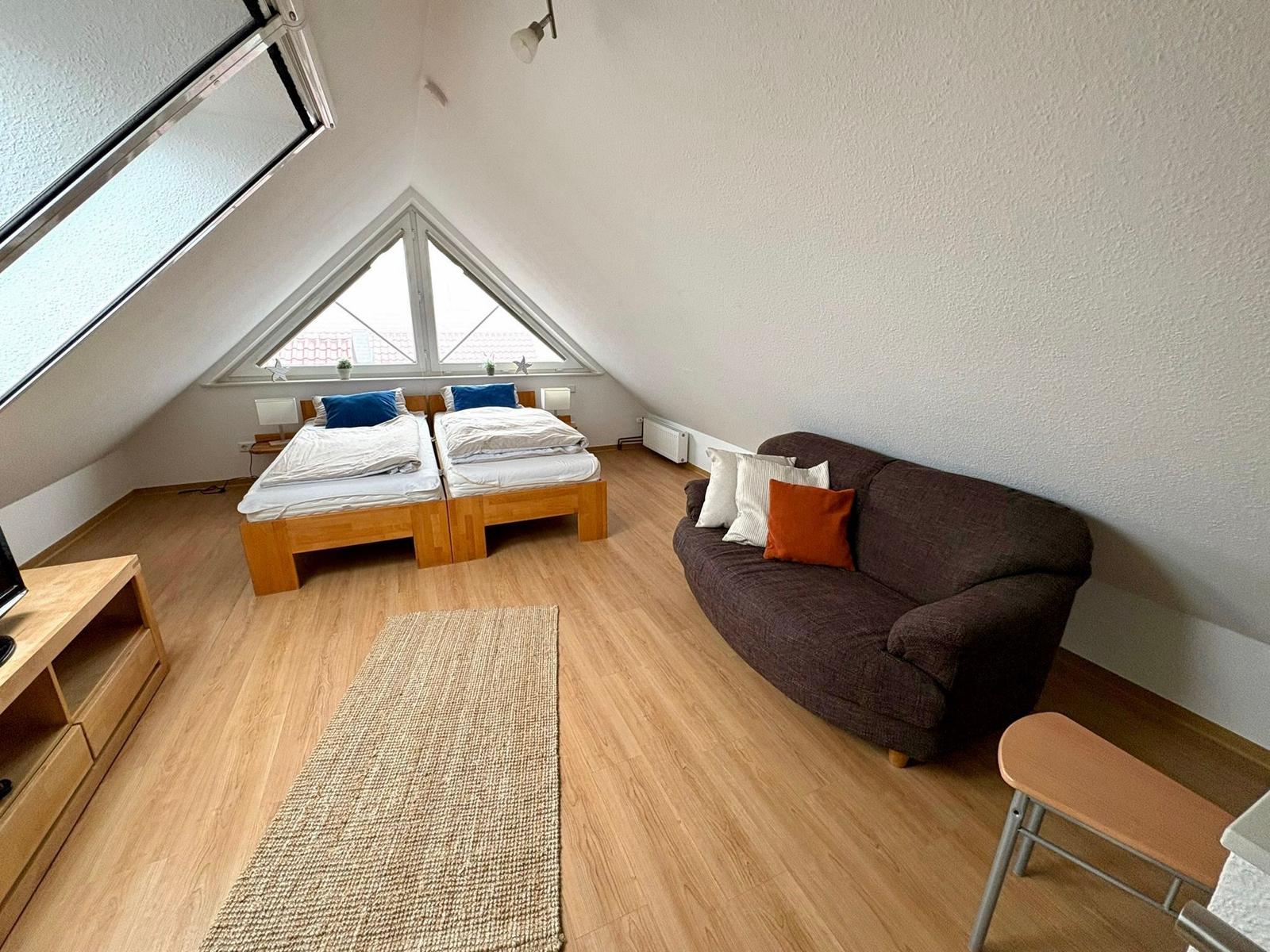 Zimmer mit zwei Betten, Sofa und Dachschrägenfenster. Holzboden und Teppich.