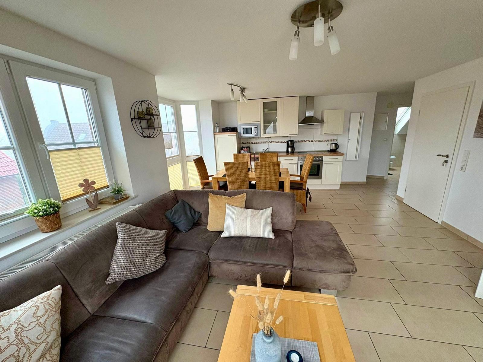 Wohn-Essbereich mit Sofa, Esstisch und Küche im Hintergrund.