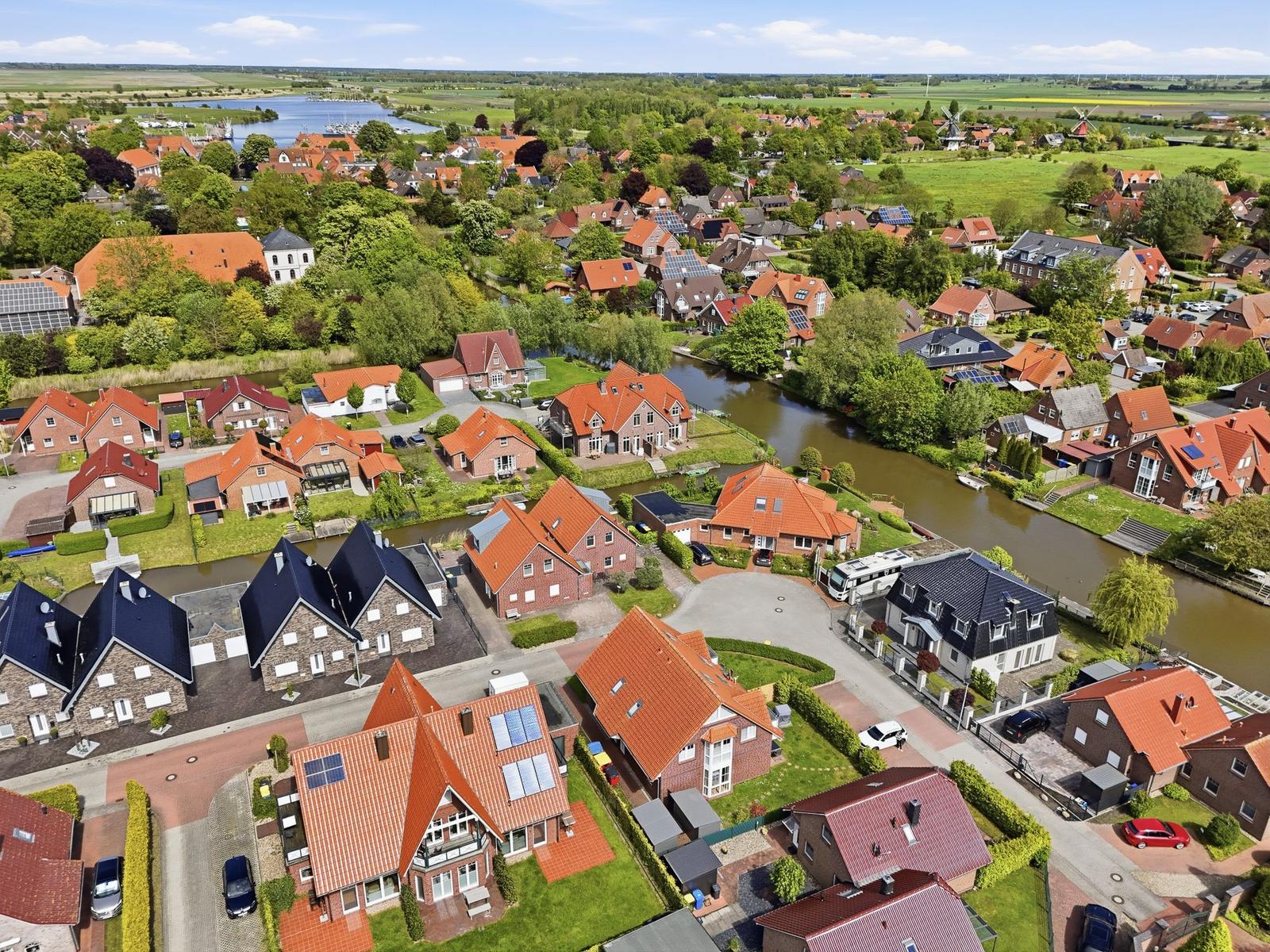 Aerial view of a village with red-roofed houses, green lawns, and a winding canal.