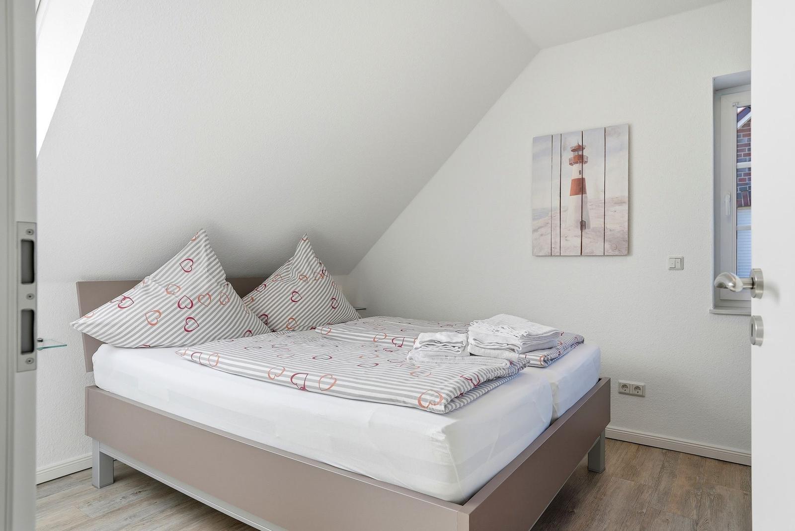 Schlafzimmer mit Dachschrägen, Bett mit Bettwäsche und Wandbild mit Leuchtturm.