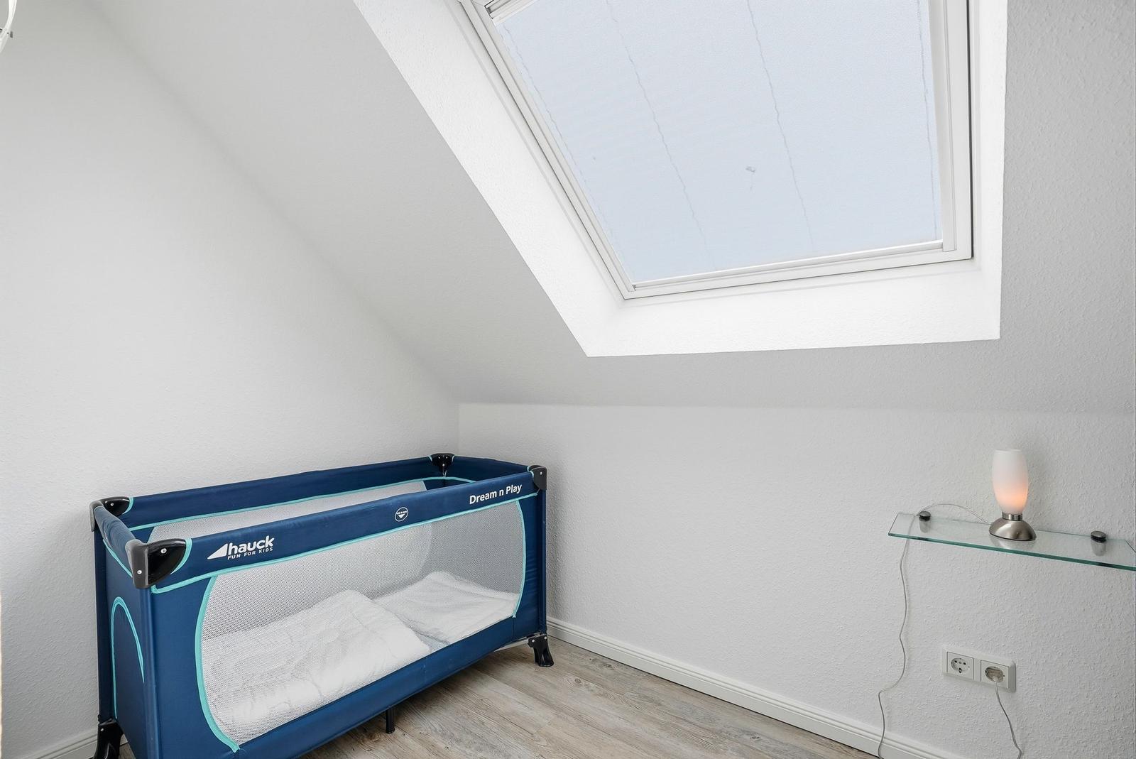 Kinderbett unter Dachschräge mit Dachfenster und Glasregal an der Wand.