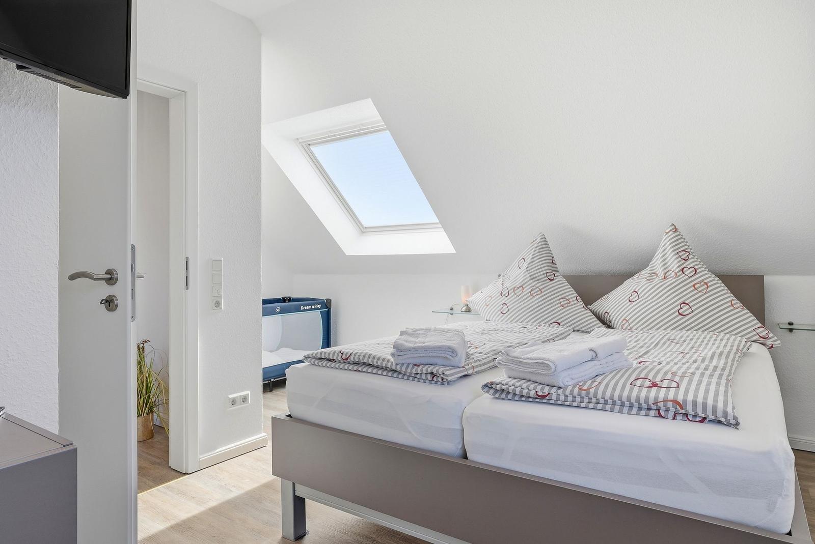 Schlafzimmer mit Dachschrägen, Dachfenster und Bett mit Bettwäsche.