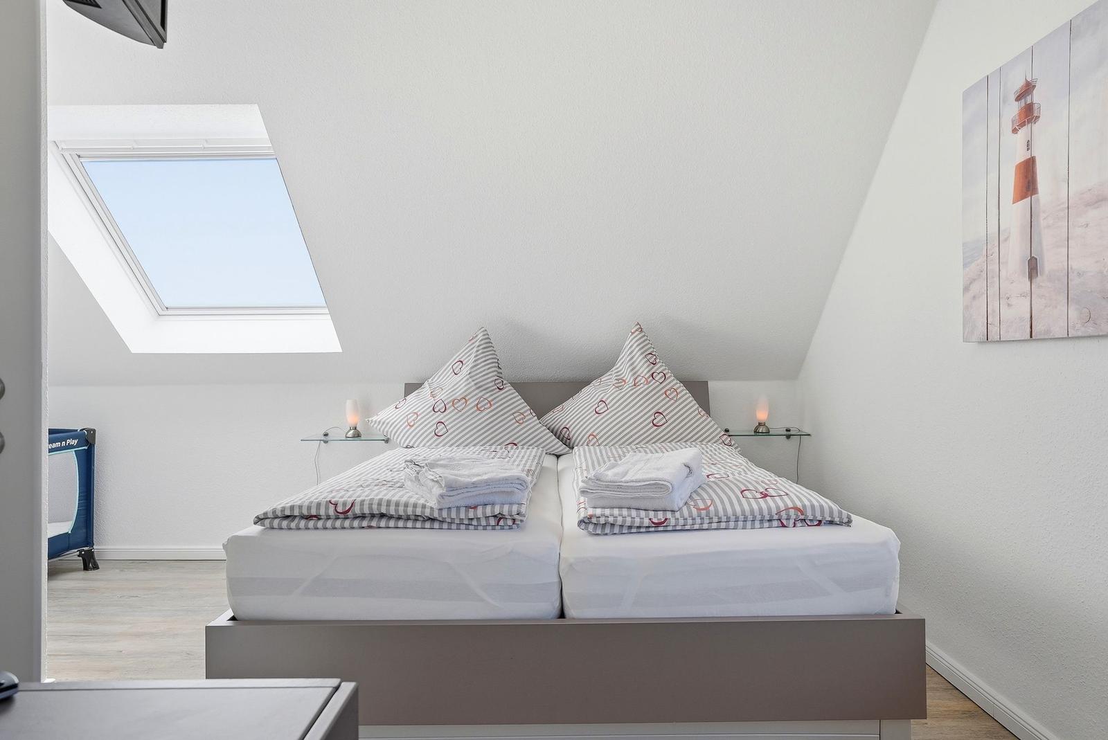 Schlafzimmer mit Doppelbett, Dachfenster und Strandmotiv an der Wand.