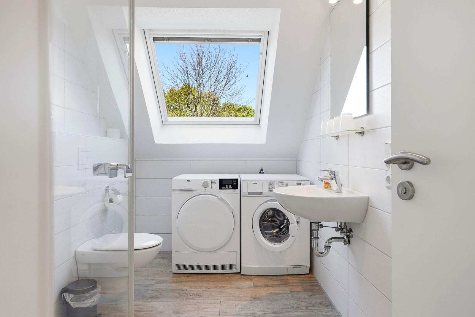 Dusche, Toilette, Waschmaschine und Trockner unter Dachfenster mit Blick auf Bäume.