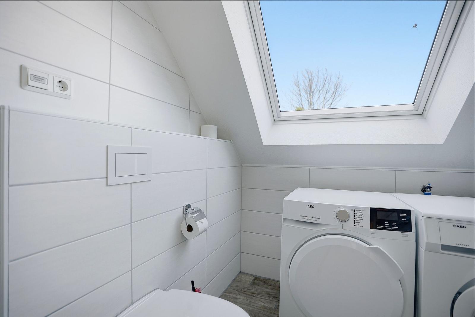 Dusche mit Waschmaschine und Dachfenster. Weiße Fliesen und Holzboden.