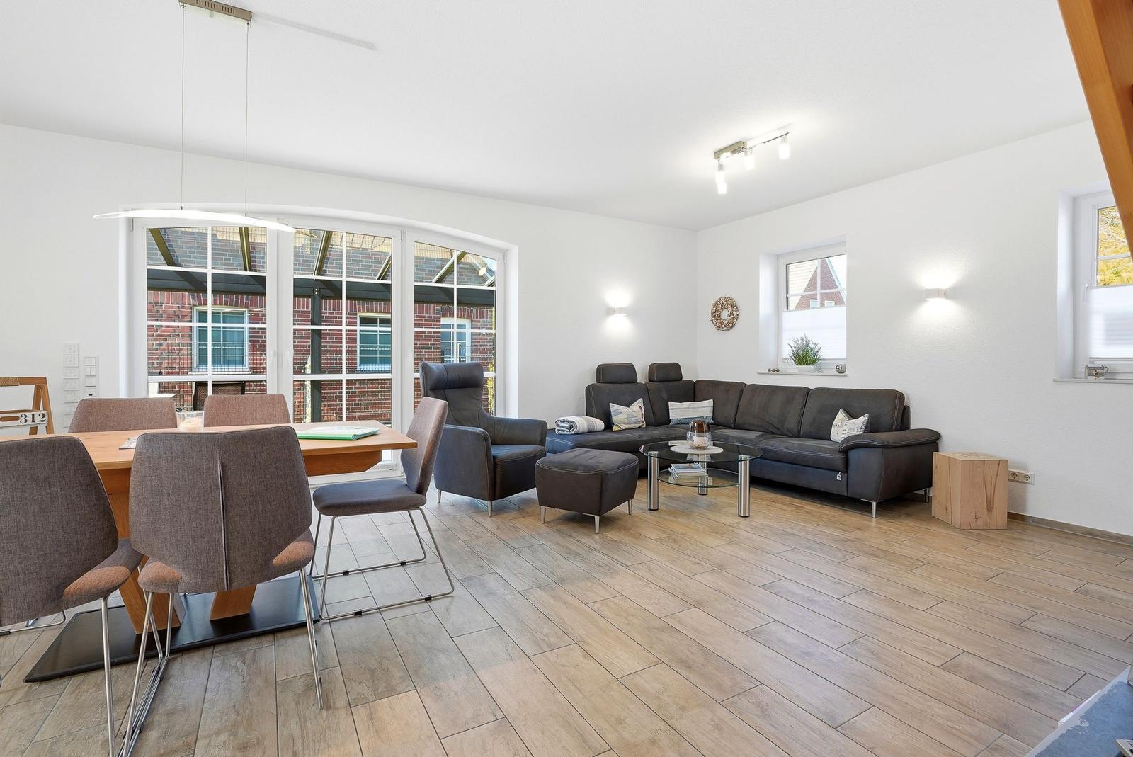 Wohn- und Essbereich mit Sofa, Esstisch und großen Fenstern.