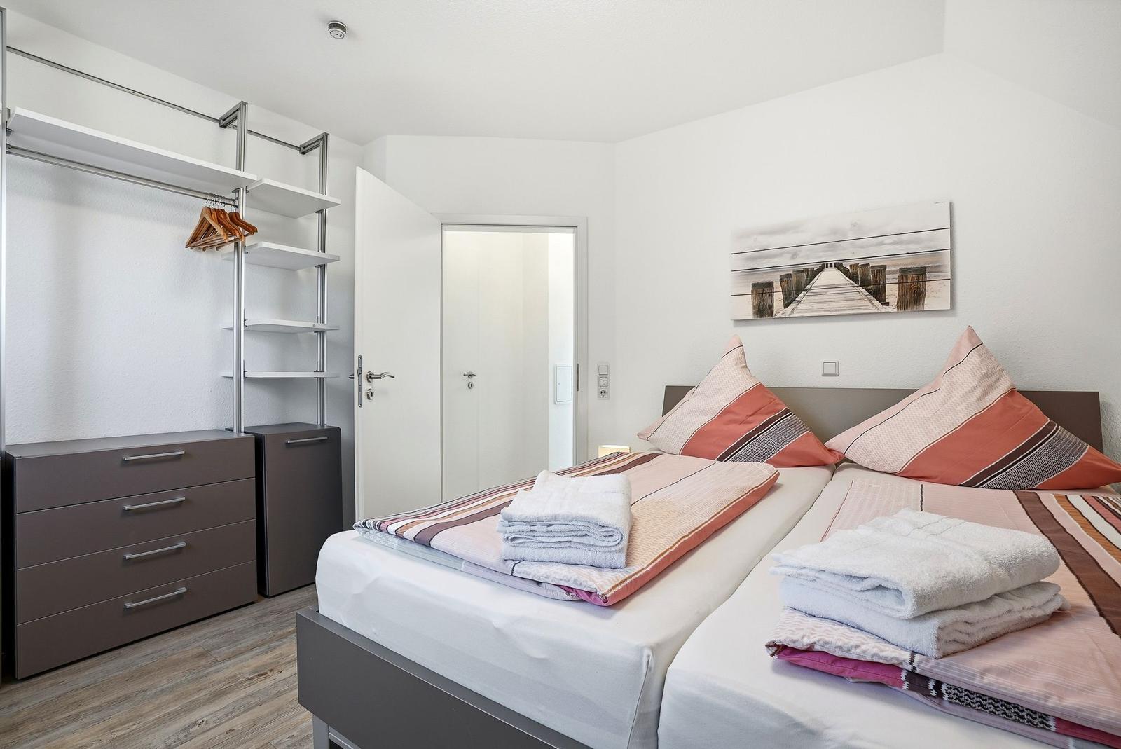 Zimmer mit Doppelbett, Kleiderschrank und Wandbild. Handtücher auf dem Bett.