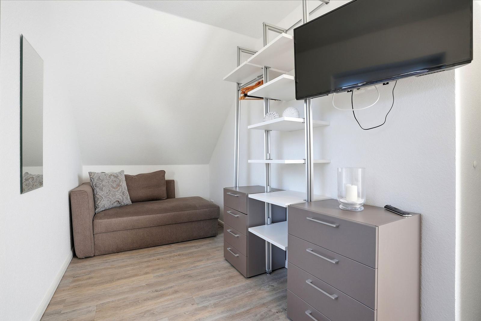 Schlafzimmer mit Sofa, Kleiderschrank und Wand-TV.