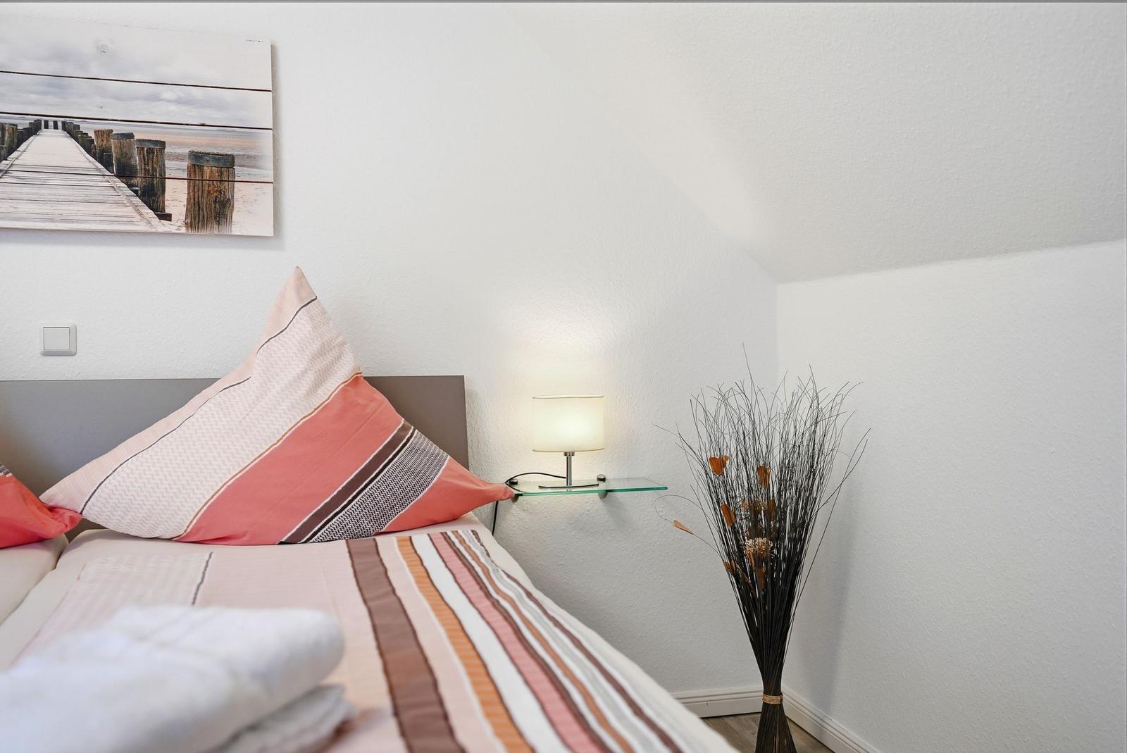 Schlafzimmer mit Bett, Wandbild und Stehlampe.