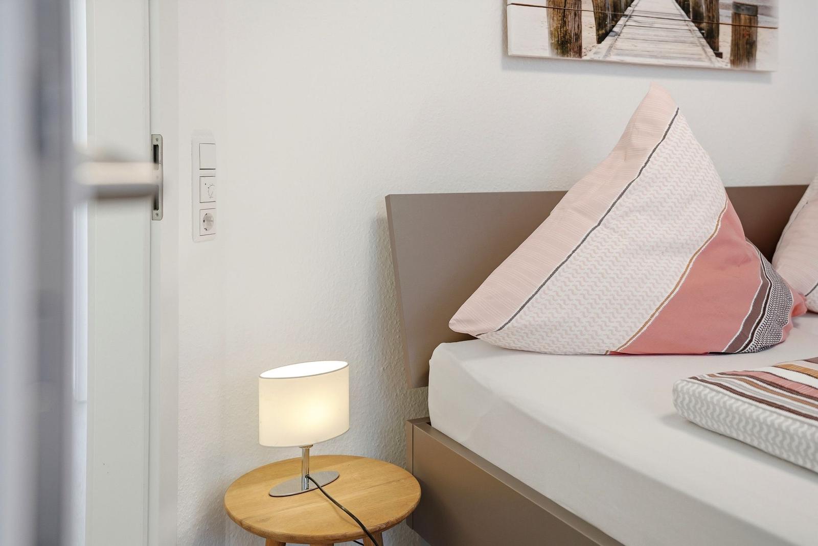 Schlafzimmer mit Bett, Nachttisch und Lampe. Wandbild und Kissen mit Streifenmuster.