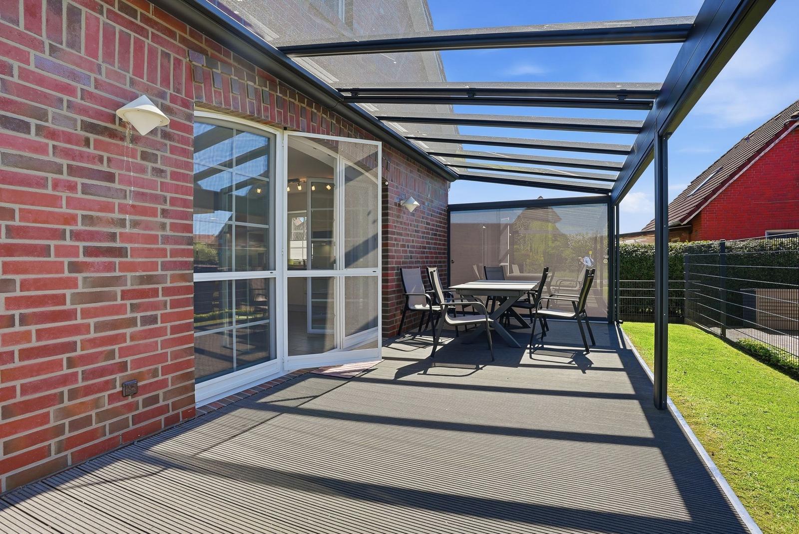 Terrasse mit Sitzgruppe unter Glasdach. Roter Backsteinbau mit Glastüren.