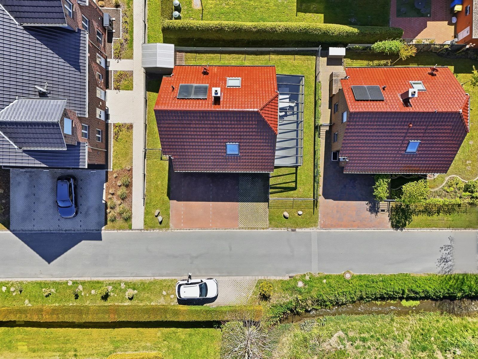 Haus mit rotem Dach, Garten und Terrasse. Straße mit Auto und Grünflächen.