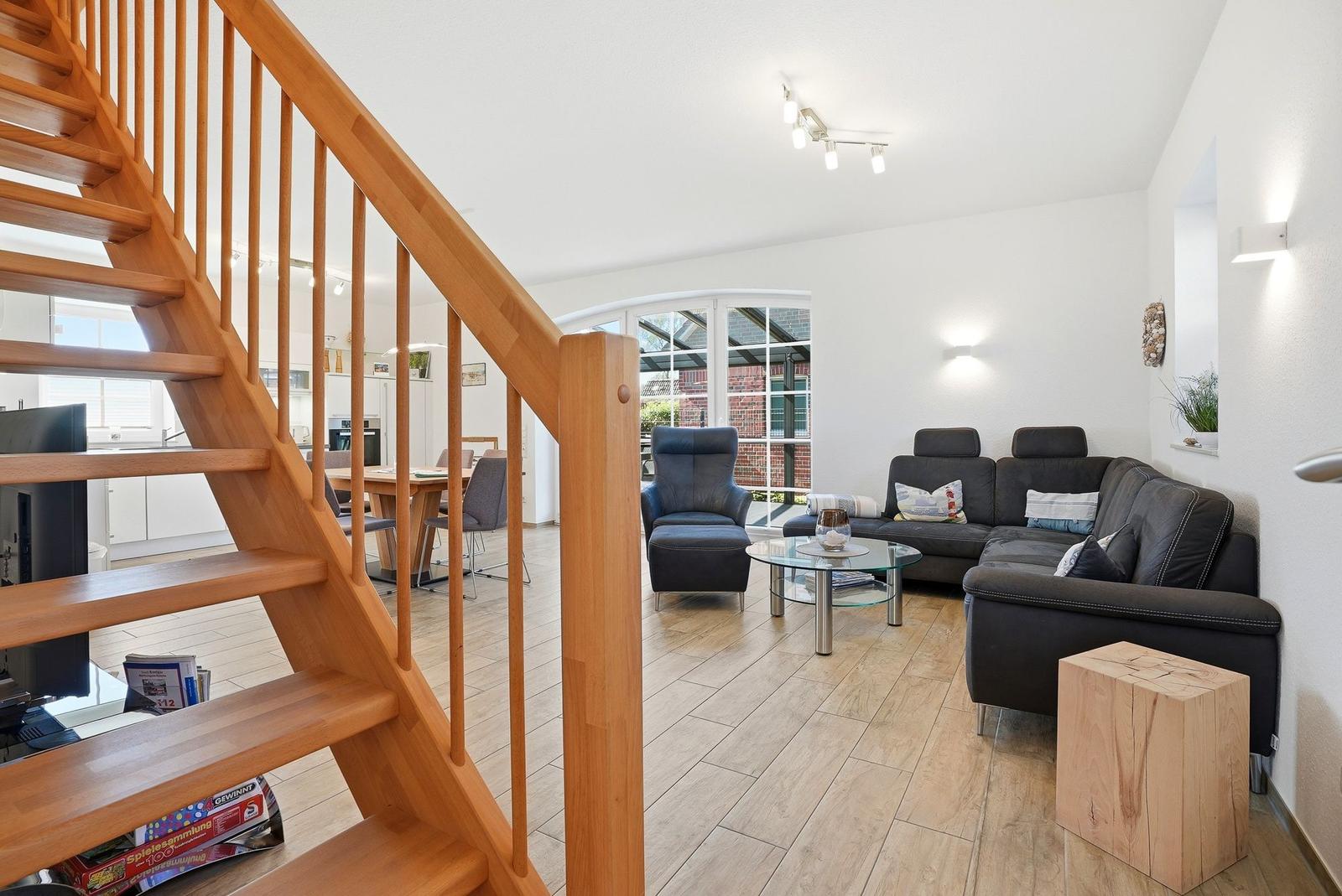 Wohnbereich mit Holztreppe, Sofa, Sessel und Glas-Tisch.