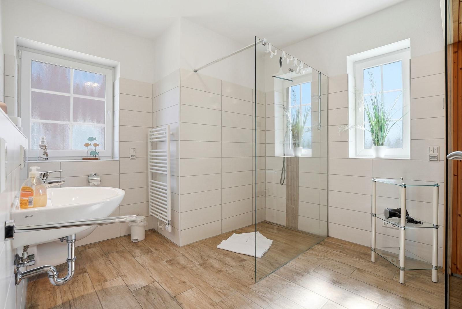 Badezimmer mit Dusche, Waschbecken und Fenstern.