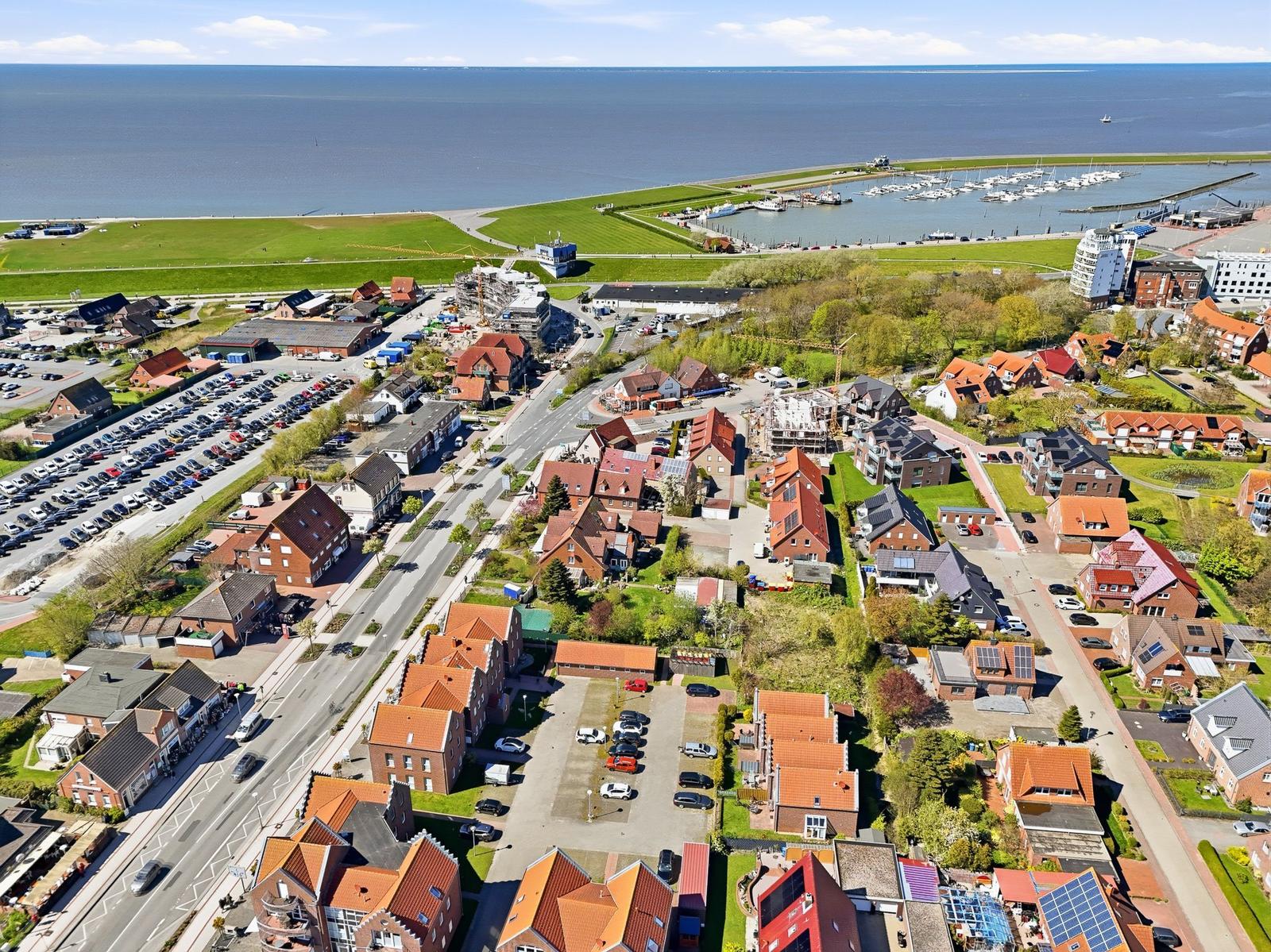 Aerial view of coastal town with marina, houses, and parking areas near the sea.
