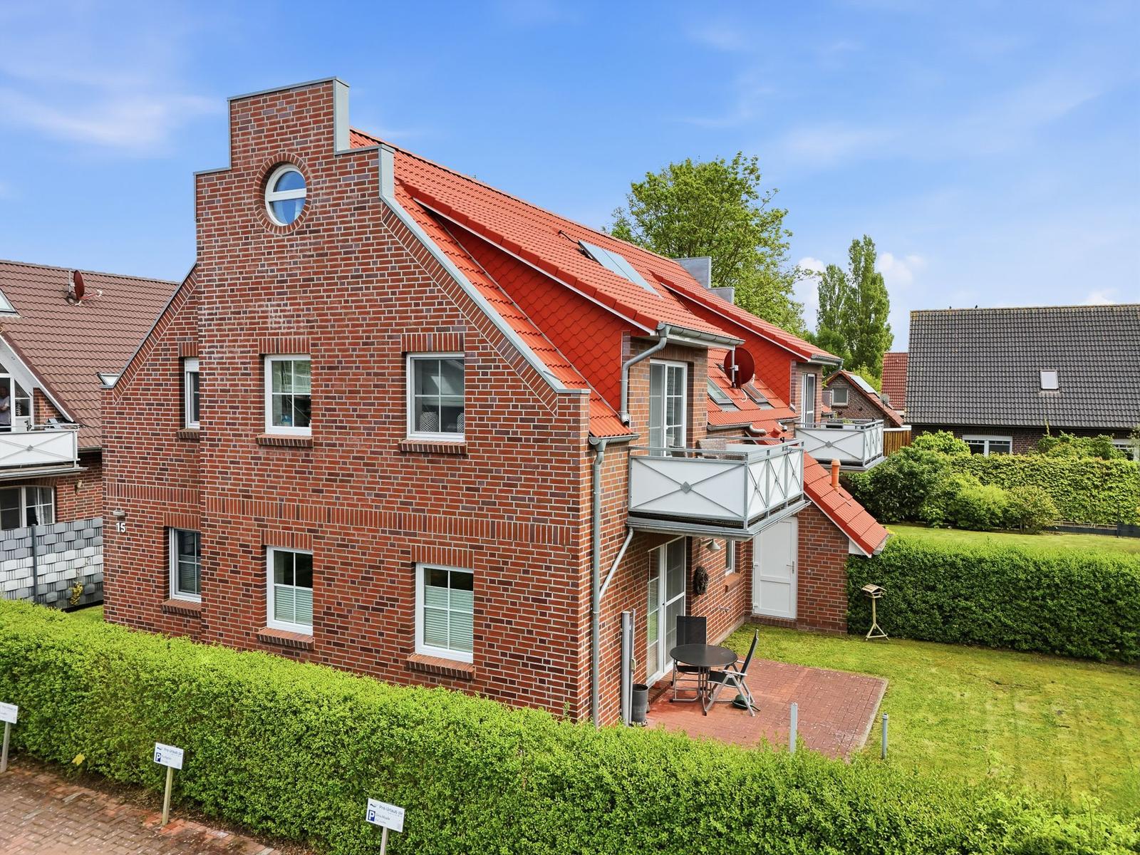 Two-story house with red roof and balcony. Front yard with lawn and hedge.