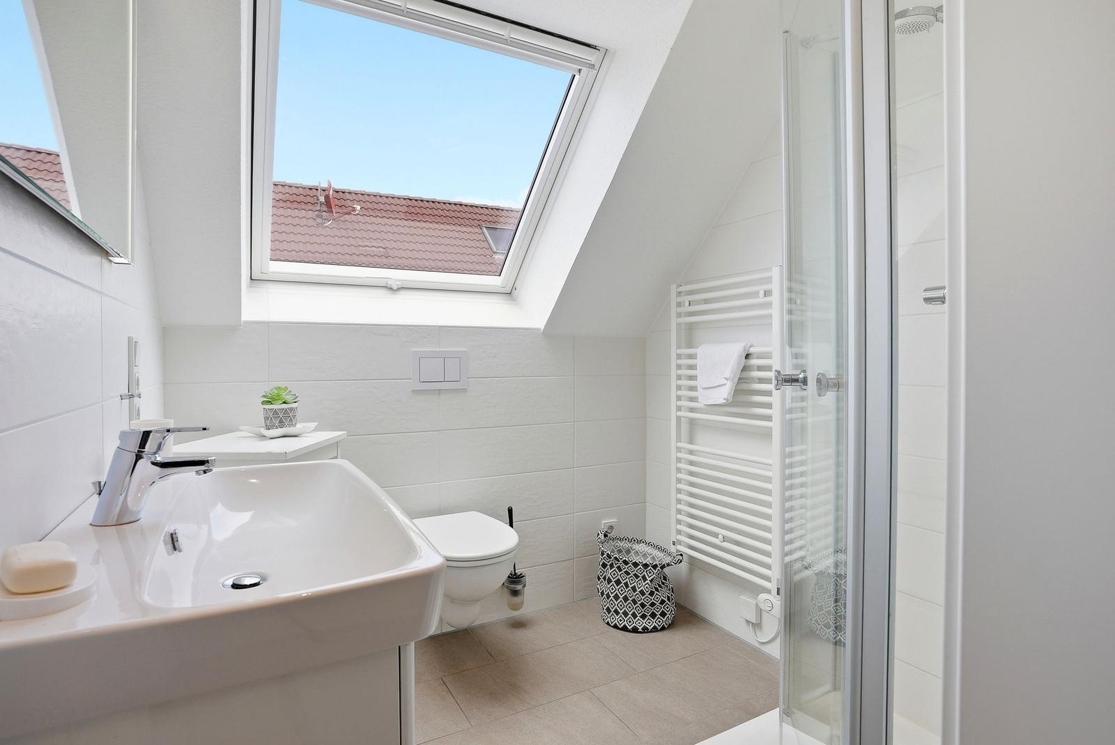 Bathroom with shower, sink, and skylight. White tiles and towel rack.