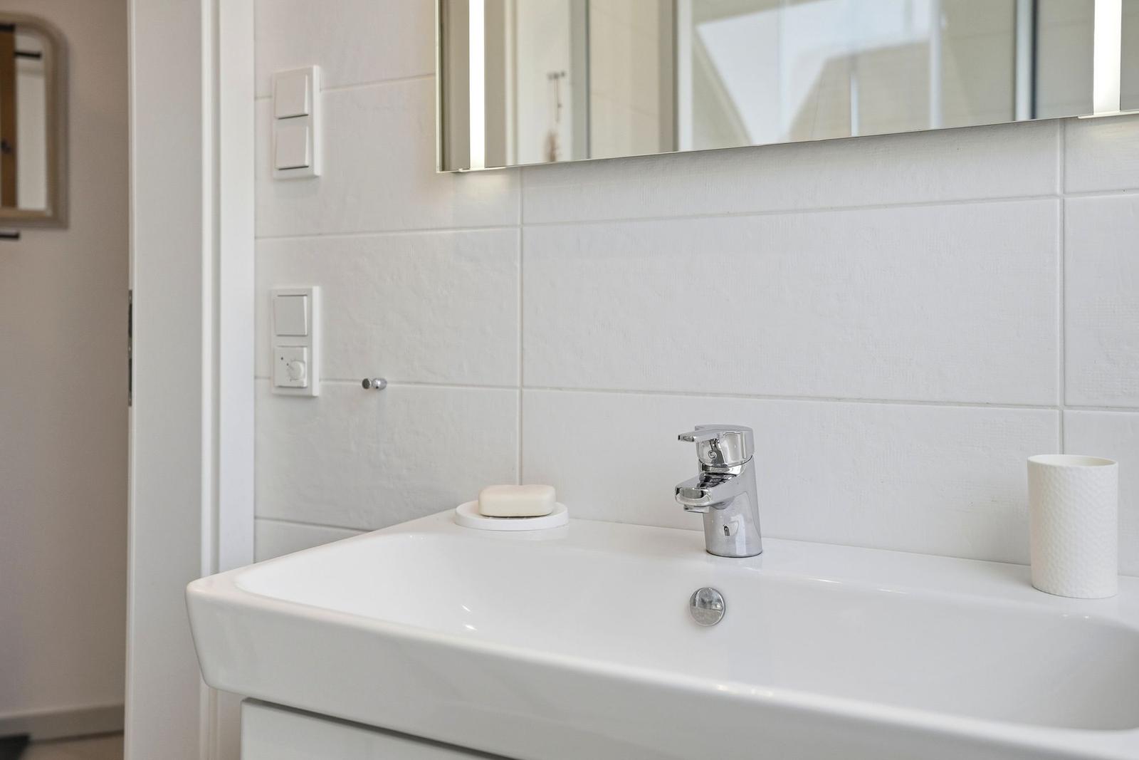 Sink with mirror and chrome faucet in white tiled wall.