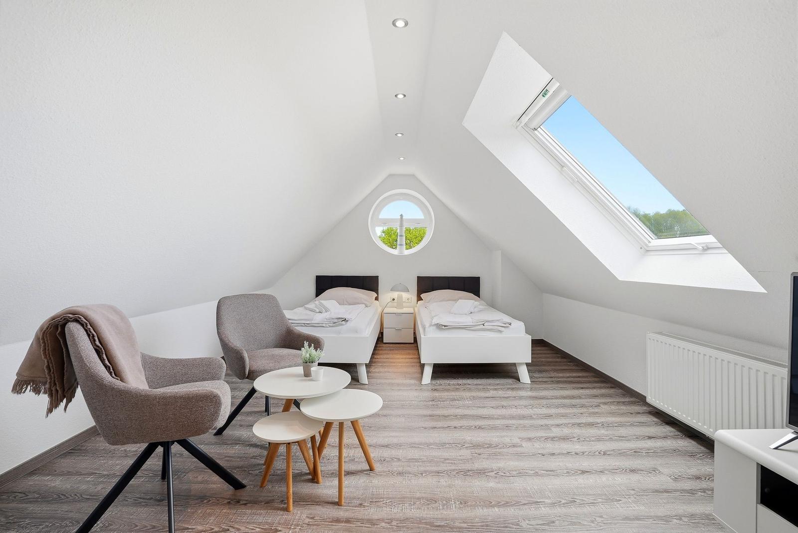 Room with two beds, seating area, and skylight. Wooden floor and white walls.
