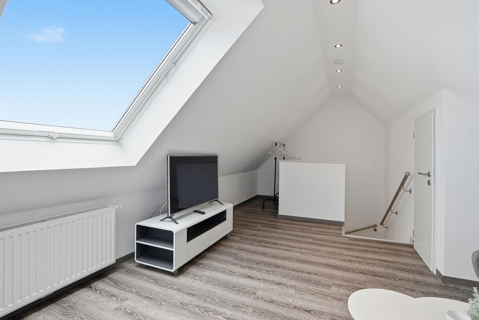 Room with sloped ceiling, TV, window, and flooring.