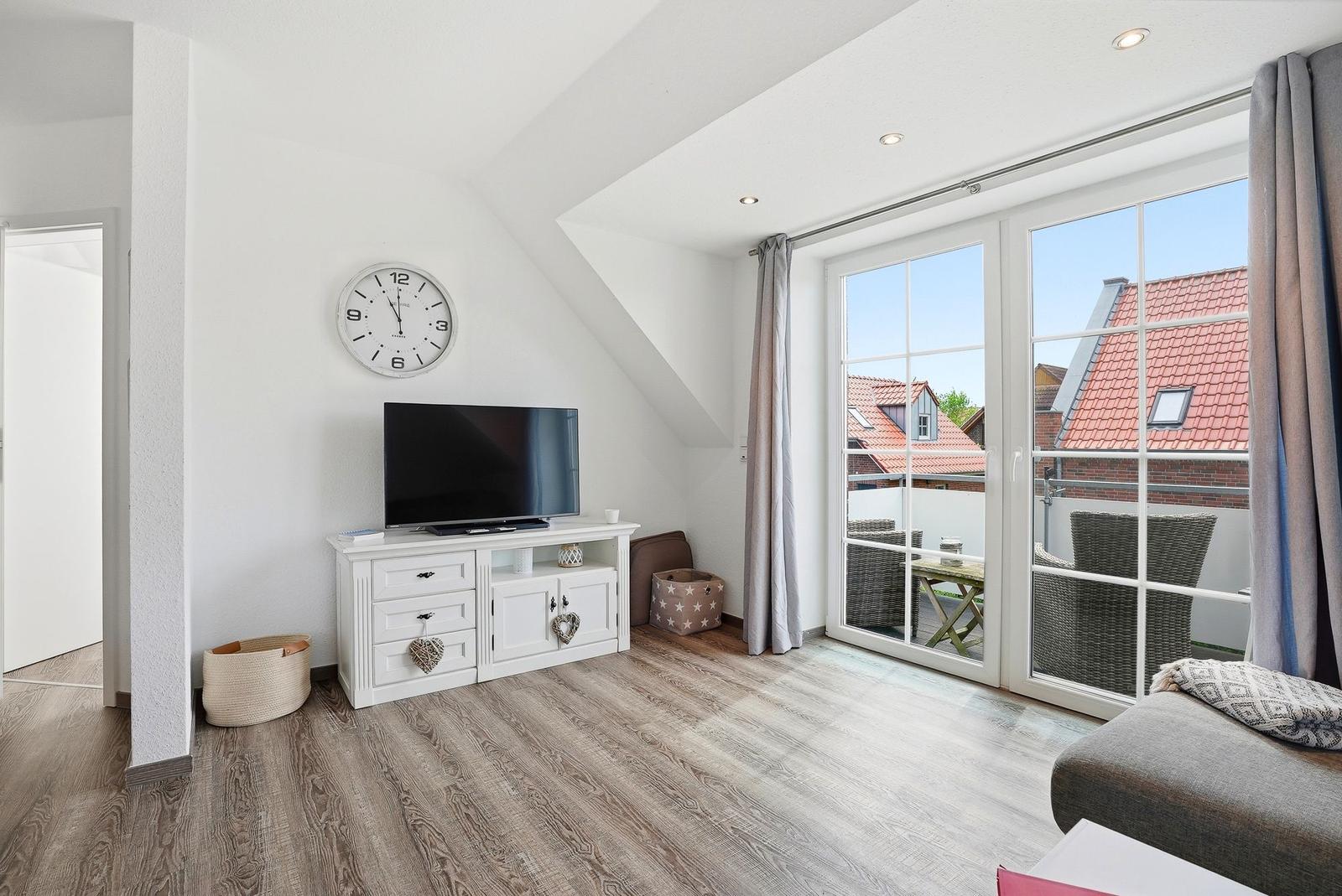 Living room with TV, cabinet, and balcony view. Wooden floor and sloped ceiling.