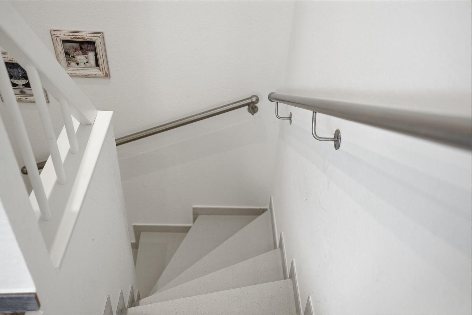 Bright staircase with metal handrails and white walls. A framed picture hangs on the wall.