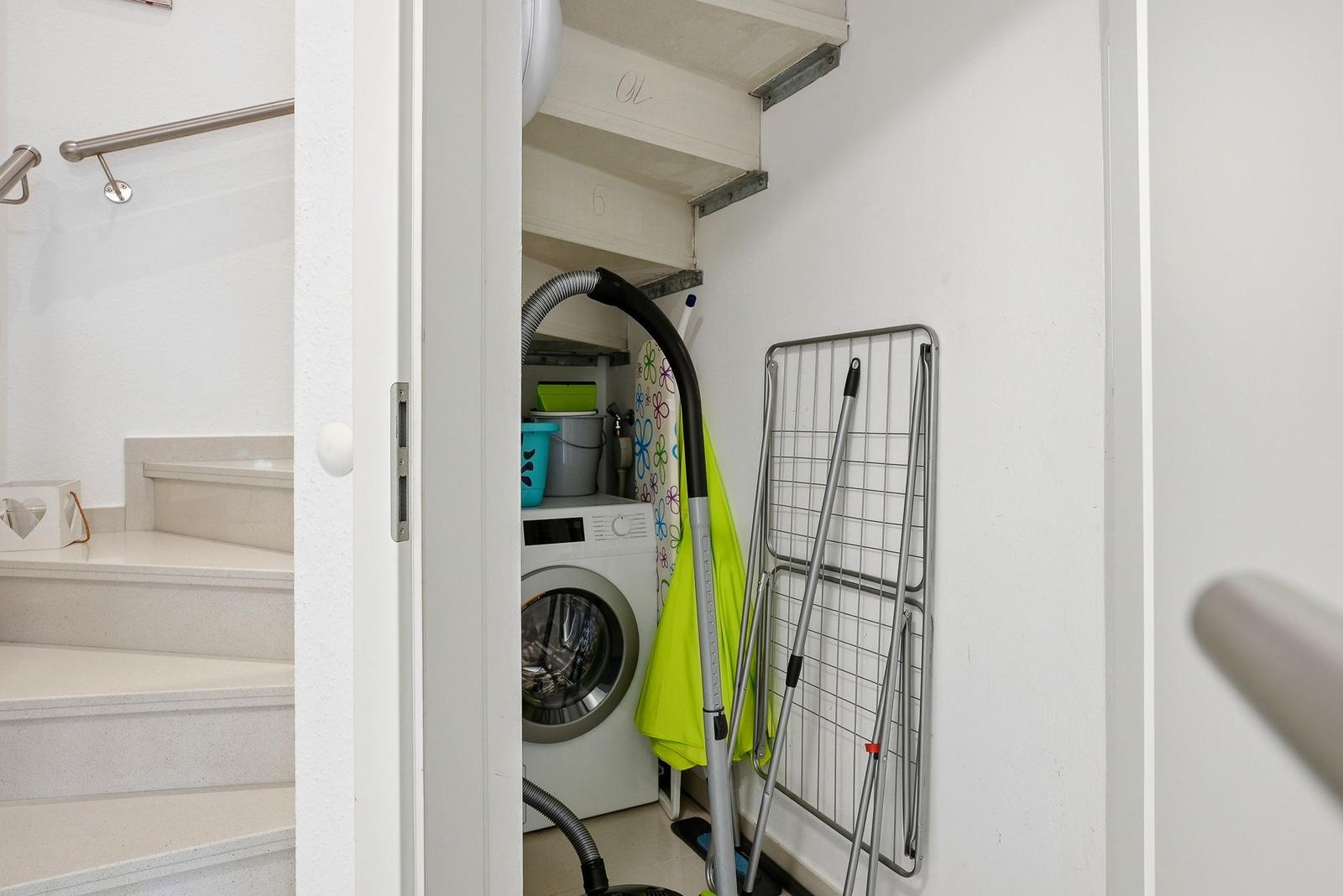 Washing machine and dryer in room with stairs and towel rack.