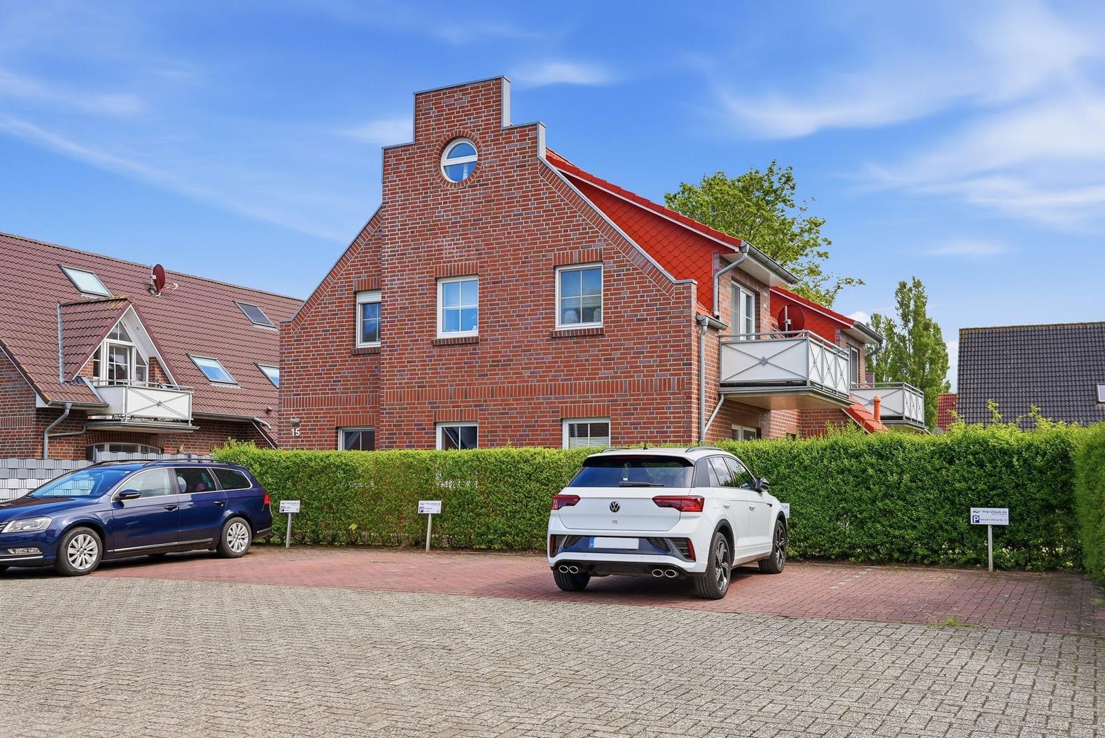 Red brick building with balcony and paved parking area.