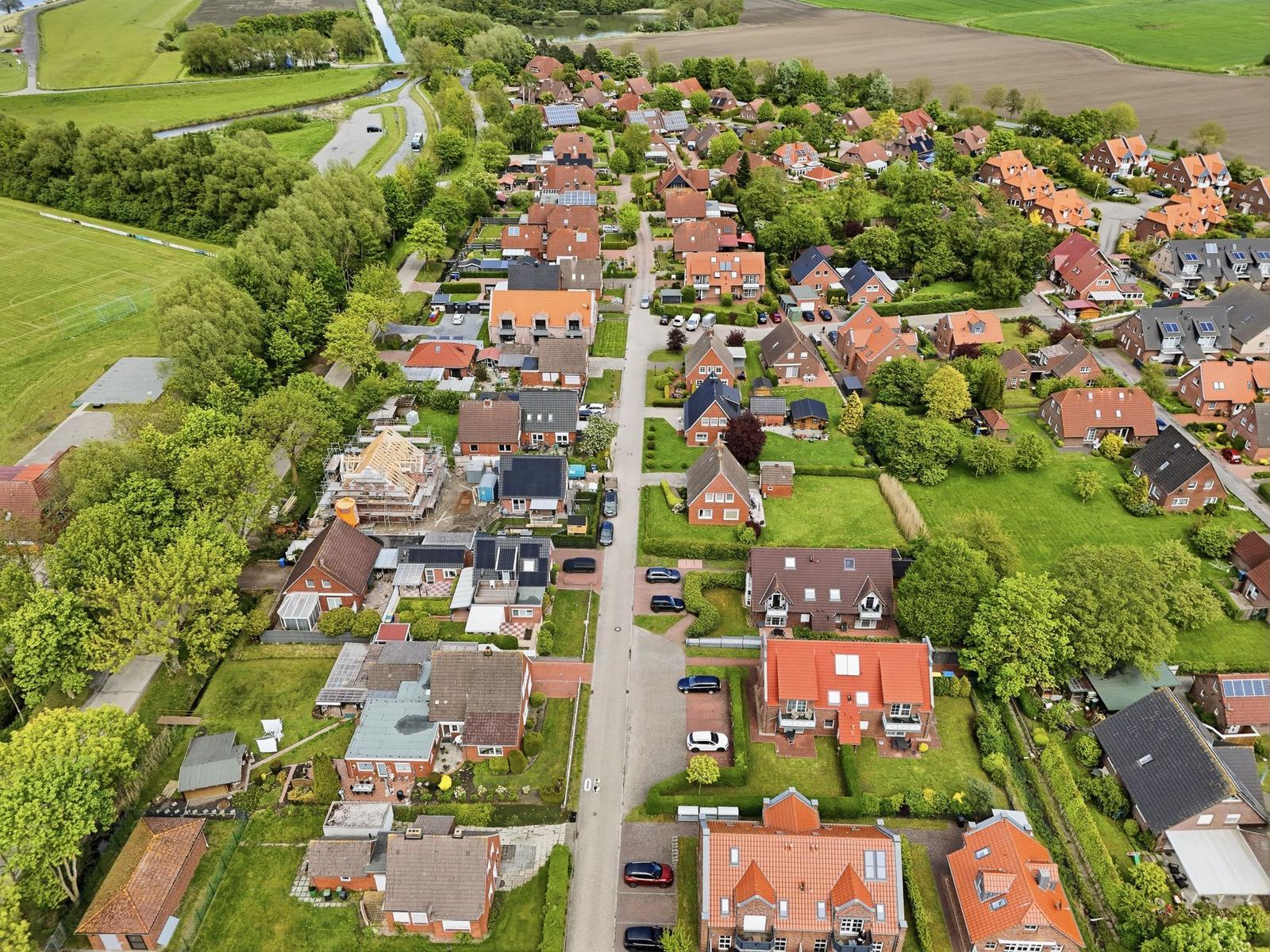 Aerial view of a residential area with houses, greenery, and a nearby field.