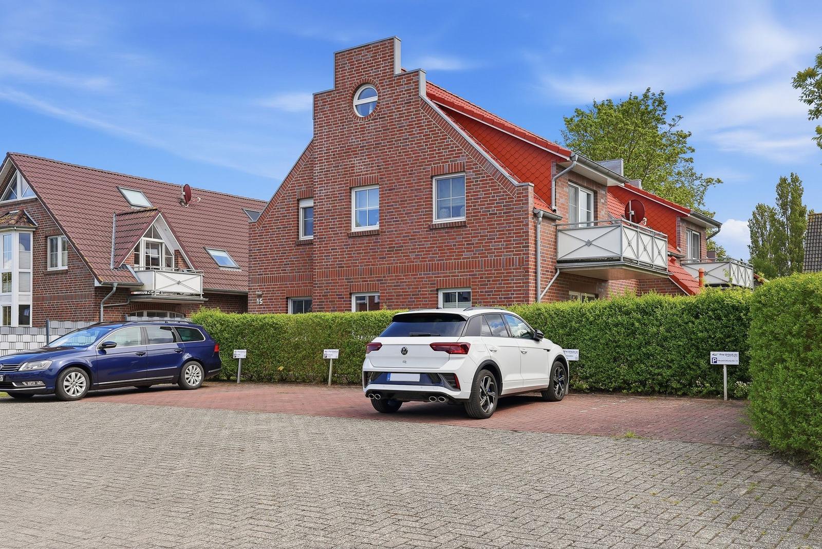 Red brick house with balconies and parking spots in front of green hedge.