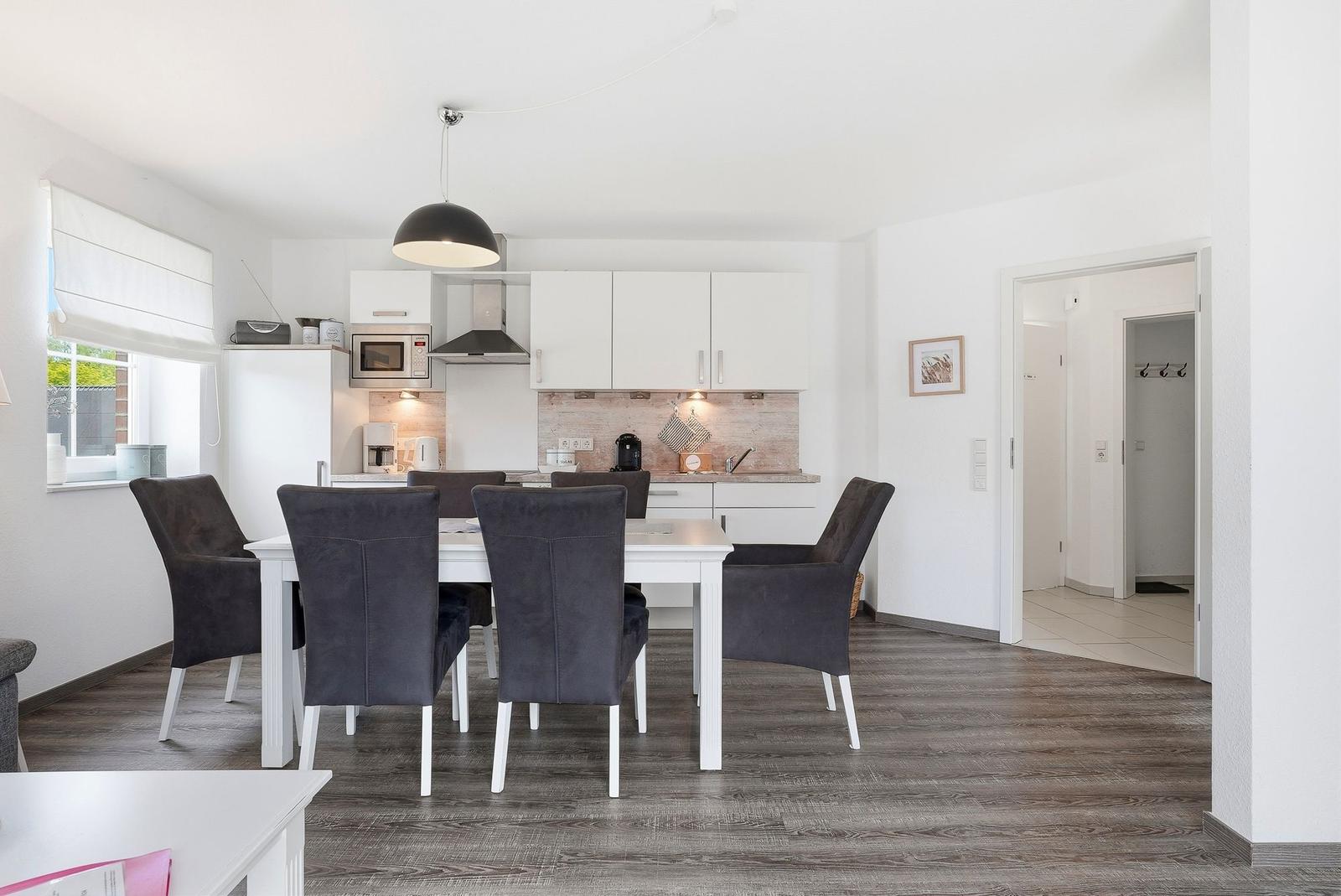 Dining area with table and chairs, kitchen with white cabinets and window