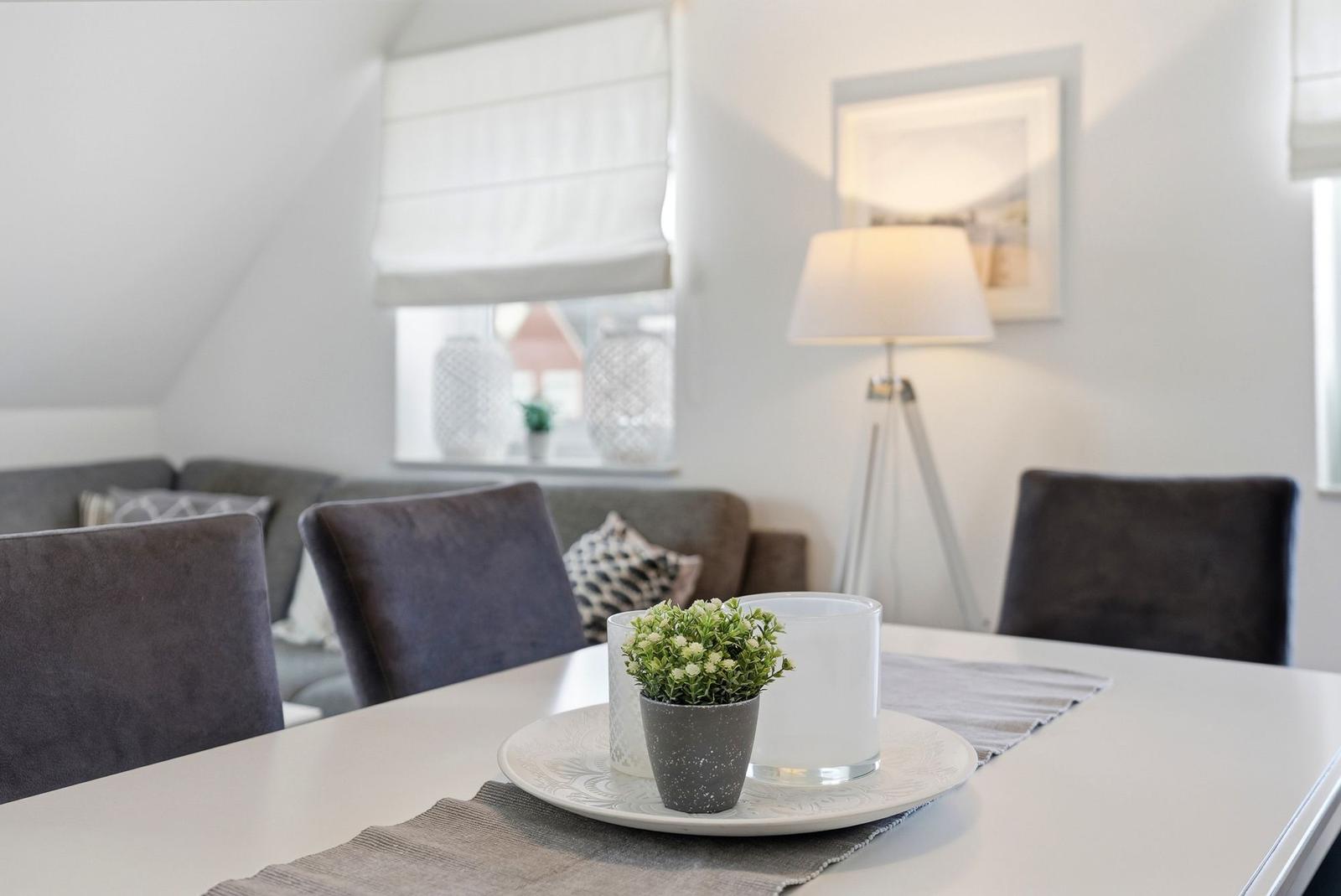 Dining table with chairs and plant. Sofa and floor lamp in background.
