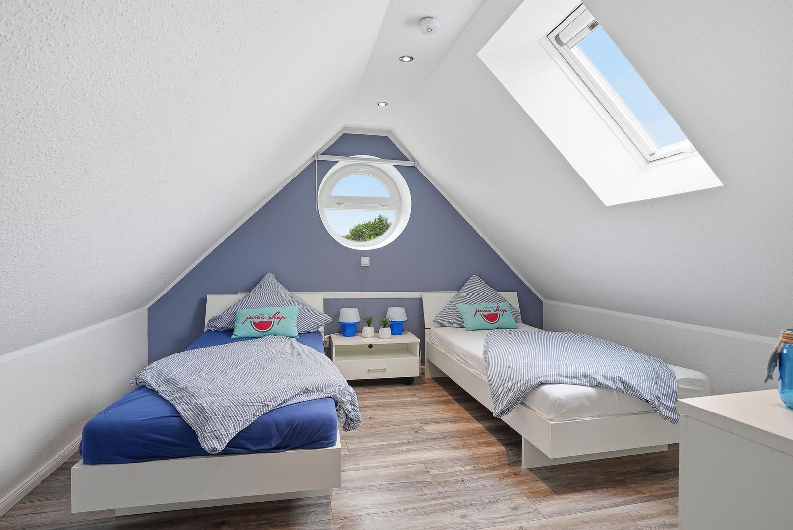Two beds in an attic room with round and skylight windows.