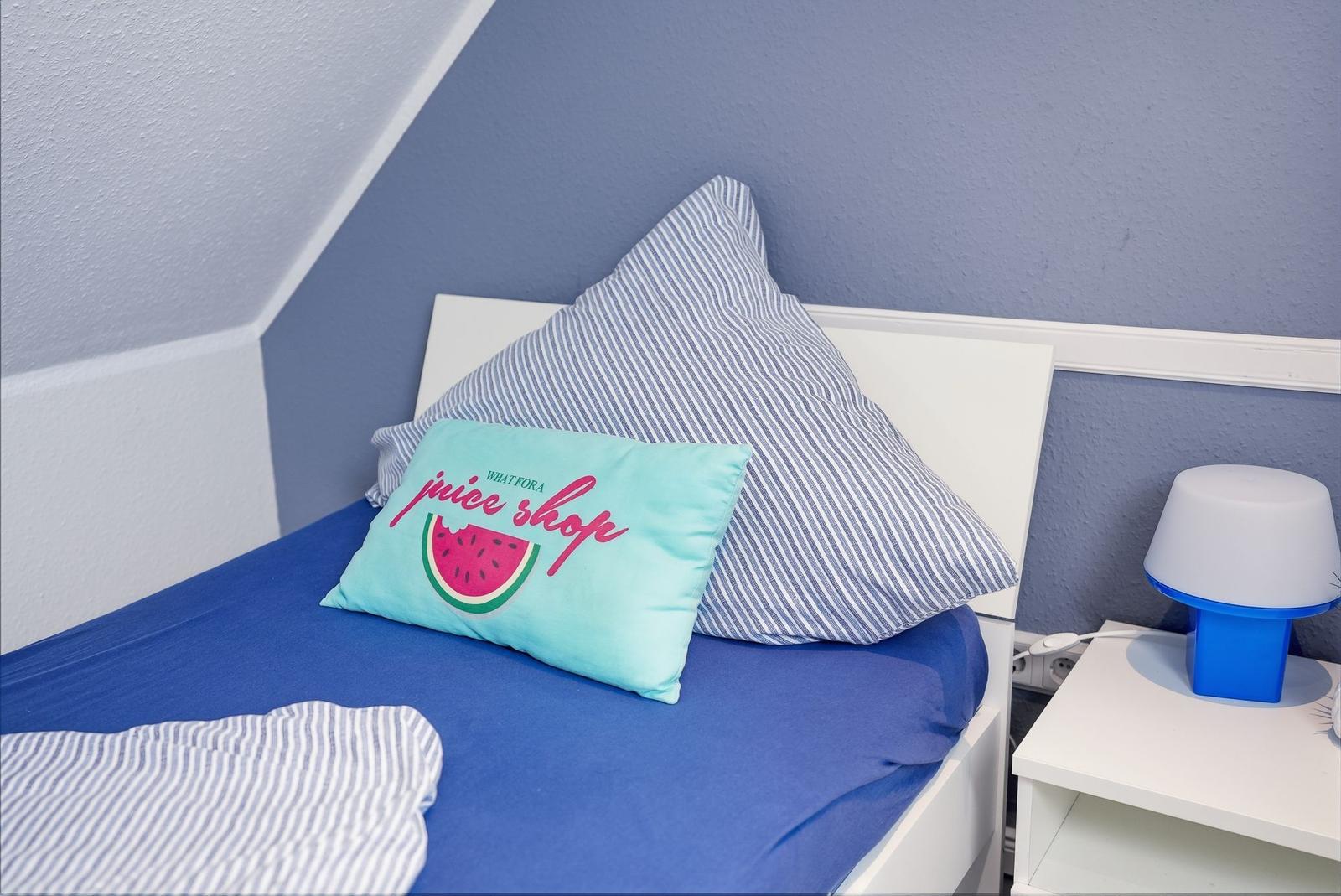 Bedroom with bed, pillows, and nightstand. Blue walls, striped duvet cover.