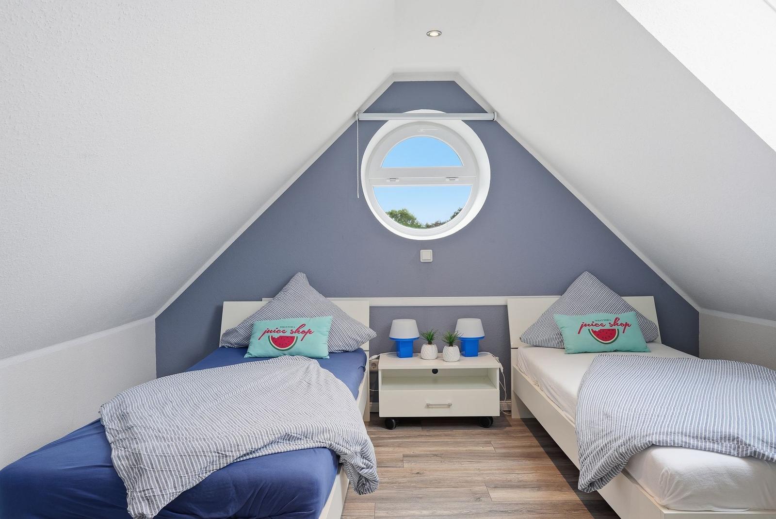 Two single beds under a skylight with blue wall and wooden floor.