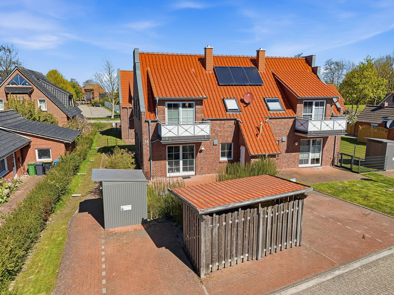 Red brick house with solar panels and balconies. Garden area with wooden shed and storage unit.