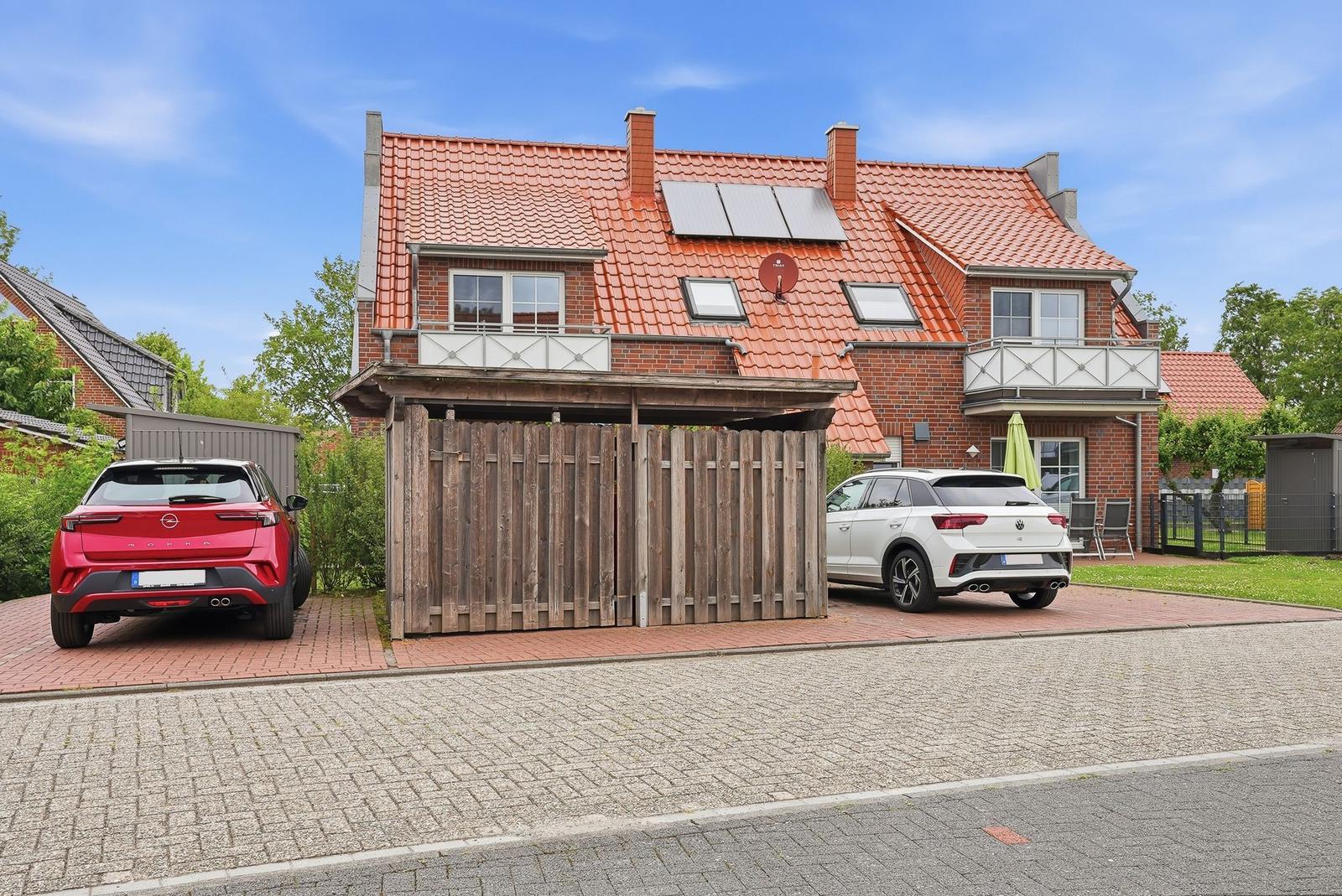 House with red roof, wooden garage, and two parked cars.