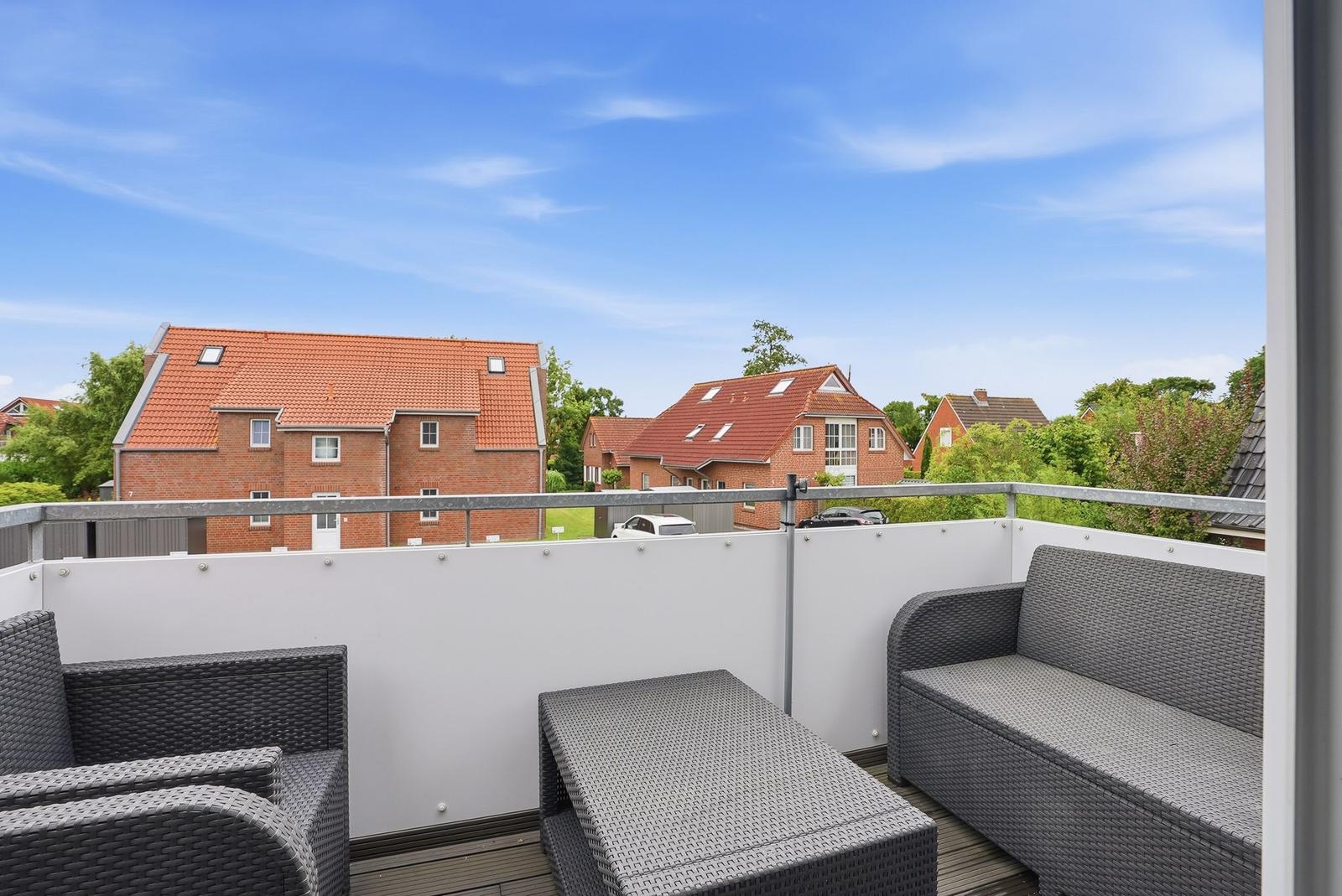 Terrace with seating group and view of houses and trees under blue sky.