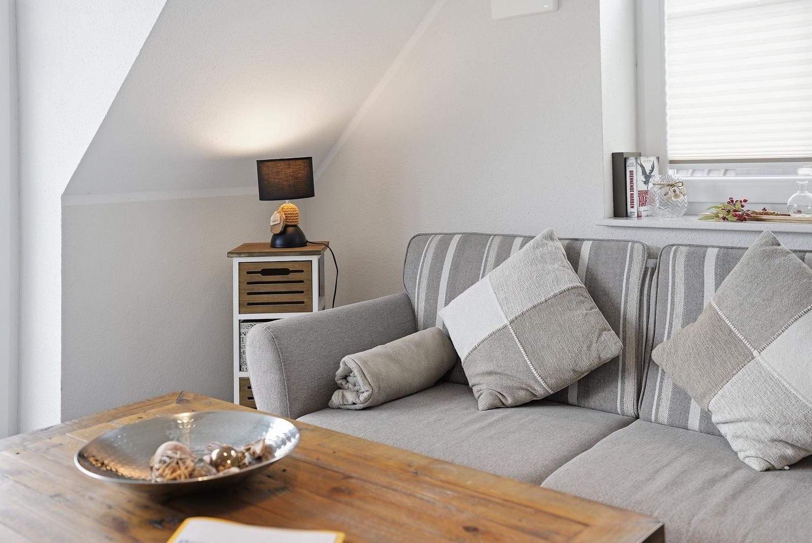 A sofa with cushions and a blanket is near a window. A bowl sits on the table.
