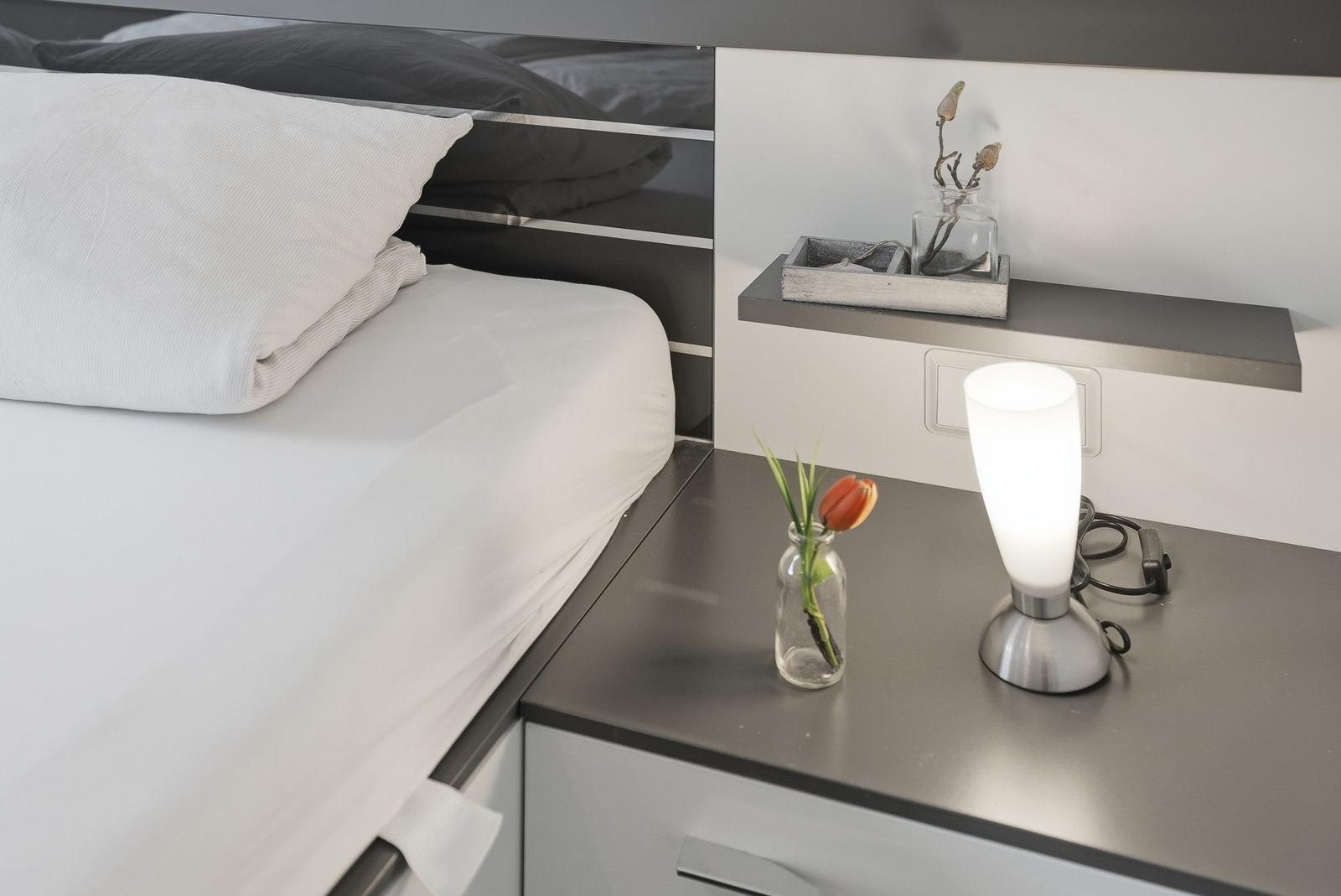Bedroom with bed, nightstand, and lamp. On the nightstand is a vase with tulip.