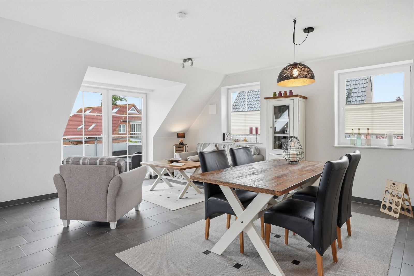 Dining room with wooden table, black chairs, and view to balcony. Living area with sofa and armchair.